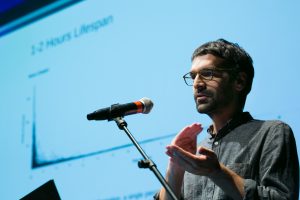 A ohoto of Vladan Joler speaking into a mic in front of a screen